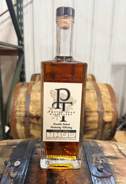 Purple Toad Double Oaked Whiskey bottle beside a wooden barrel.